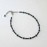 Black beaded anklet with silver accents and a chain attachment.