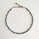 Adjustable black ankle bracelet with multicolored beads and a metallic clasp.