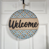 A round wooden 'Welcome' door sign with a blue oval frame and a sisal rope hanger.