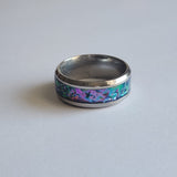 Hand-turned dichroic resin ring on a stainless steel band, shifting purple, blue, and green in the light.