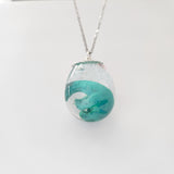 Resin dinosaur encased in clear egg pendant on stainless steel chain