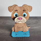A wooden eyeglass holder in the shape of a cartoon dog wearing eyeglasses, with a blue base.