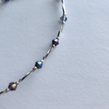 Ankle bracelet with silver tube and iridescent blue beads.