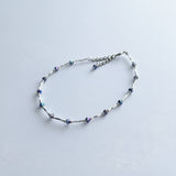 Ankle bracelet with silver tube and iridescent blue beads.